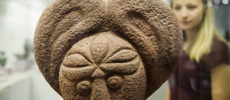 Kopf einer Steinskulptur mit Besucherin im Hintergrund