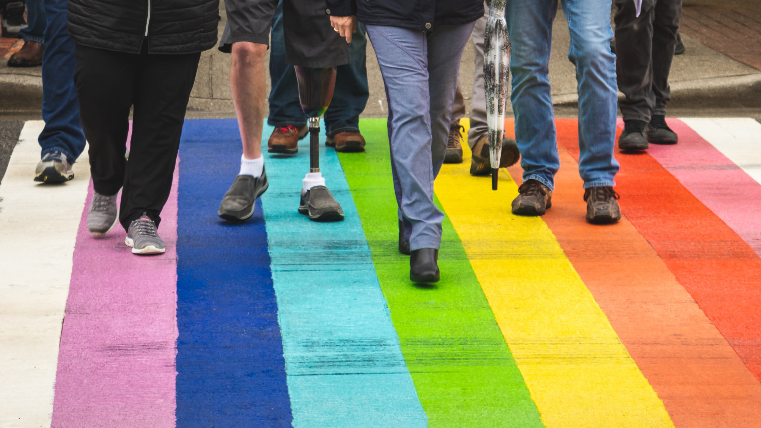 greg-rosenke-c-unsplash Menschen laufen über eine Straße, die in den Regenbogenfarben bemalt ist.
